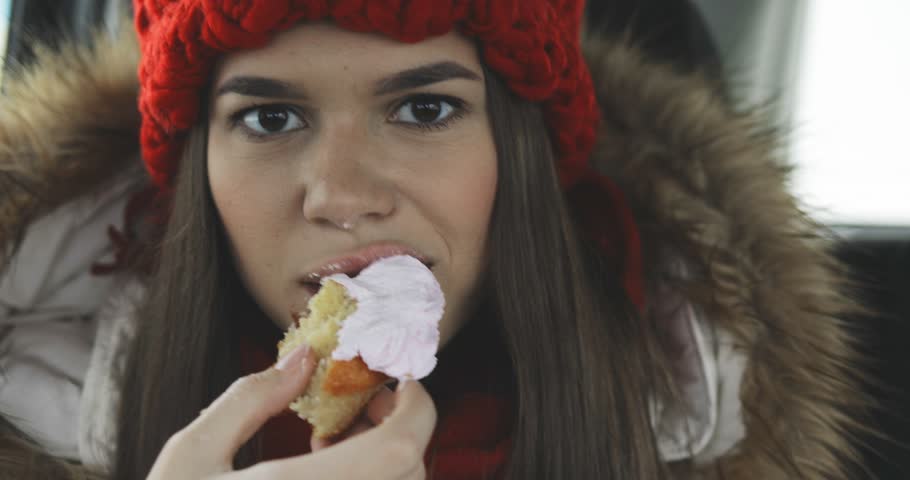 happy pretty beautiful girl or woman finishing eating delicious cake (cupcake), smiling, wearing winter outfit