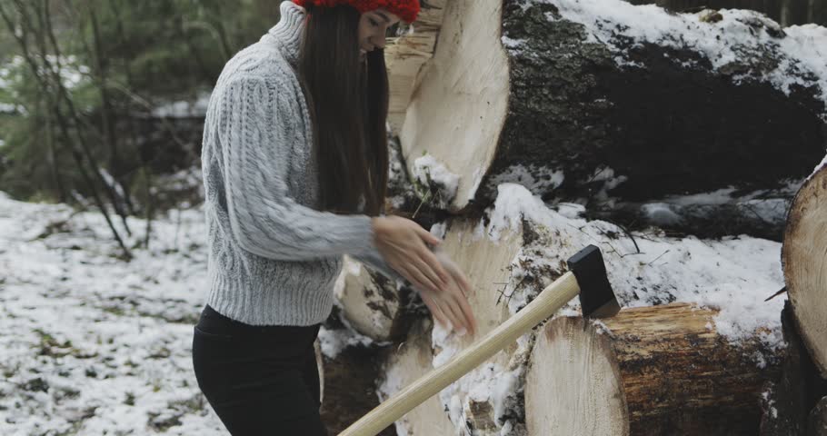 sexy young woman or girl / lumberjack getting out of log or timber ax (axe, hatchet) and walking away. winter snowy forest on background