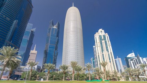 The skyline of Doha seen from Park timelapse hyperlapse, Qatar. Trees and palms on foreground. Mordern skyscrapers and towers on background. Traffic on road