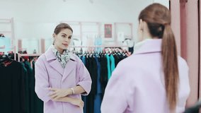 Young slim lady with ponytale trying on a coat. Woman shopping and checking pink coat in front of mirror. Style and fashion concept