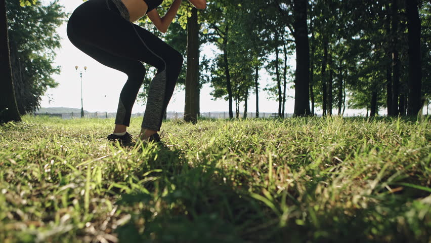 Athletic woman doing squats during training in park on sunny day