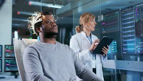 In Laboratory Man Wearing Brainwave Scanning Headset Sits in a Chair while Scientist with Tablet Computer Supervises Process. In the Modern Brain Study.  Shot on RED EPIC-W 8K Helium Cinema Camera. - Powered by Shutterstock - Get 15% off with code: PIKWIZARD15
