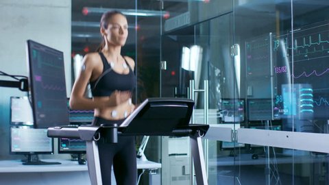 Beautiful Woman Athlete Runs on a Treadmill with Electrodes Attached to Her Body, Female Physician Uses Tablet Computer and Controls EKG Data Showing on Monitors. Shot on RED EPIC-W 8K  Camera.