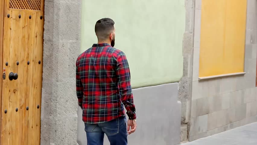 Man on red checkers flannel shirt and blue jeans walking alone down pedestrian street. City tour visit on empty avenue with colorful buildings in old town Vegueta, Las Palmas