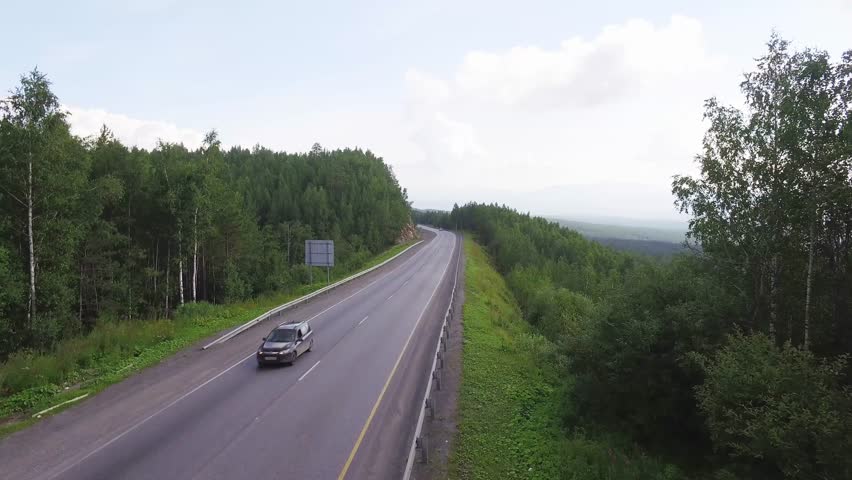 One white truck driving along the freeway amidst a dense forest in the mountains. Summer, sunny, beautiful sky with clouds. Aerial drone view. Royalty-Free Stock Footage #1007618764