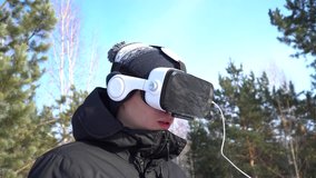 a young man in a jacket, in a hat, in glasses of virtual reality against the background of nature