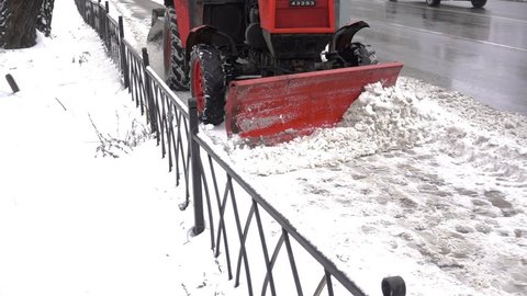Slow Motion of compact tractor with snow-removing equipment cleans street pavement from snow.