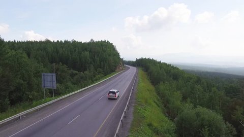 One small gray car rides a forest freeway in the Ural Mountains at summer sunny day - Aerial drone view