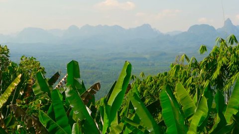 View of the valley with mountains in the background. Rocks on the horizon with banana palm leaves in the foreground. Typical Asian Landscape. Virgin nature of the southeast asia. Thailand.