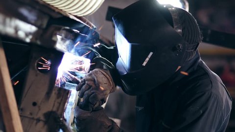 Male worker at a welding factory in a welding mask. Welding on an industrial plant. Slow motion.