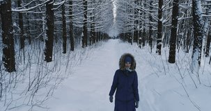 Aerial video of woman in warm clothes walking in the winter forest alley, look side by side.