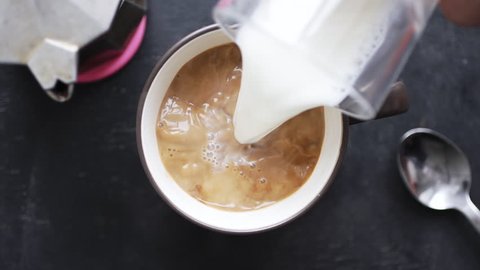 Top view slow motion of milk being poured into coffee