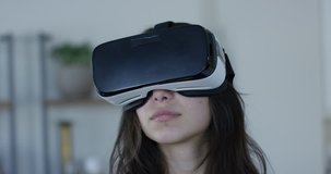 Young hip woman wearing VR 360 goggles in living room - moving head around virtual space