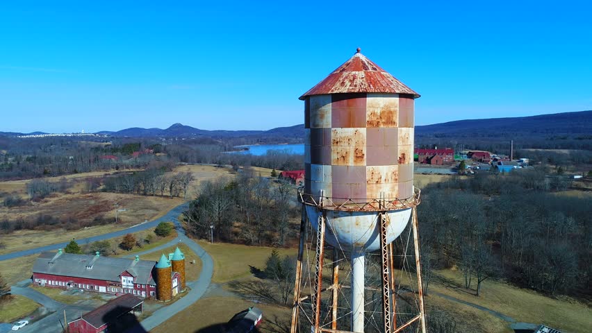 This is an aerial view of two water towers.  One is a modern blue water tower - and the other is an old, rusty checkerboard water tower.  The water towers are located in Warwick, New York. 