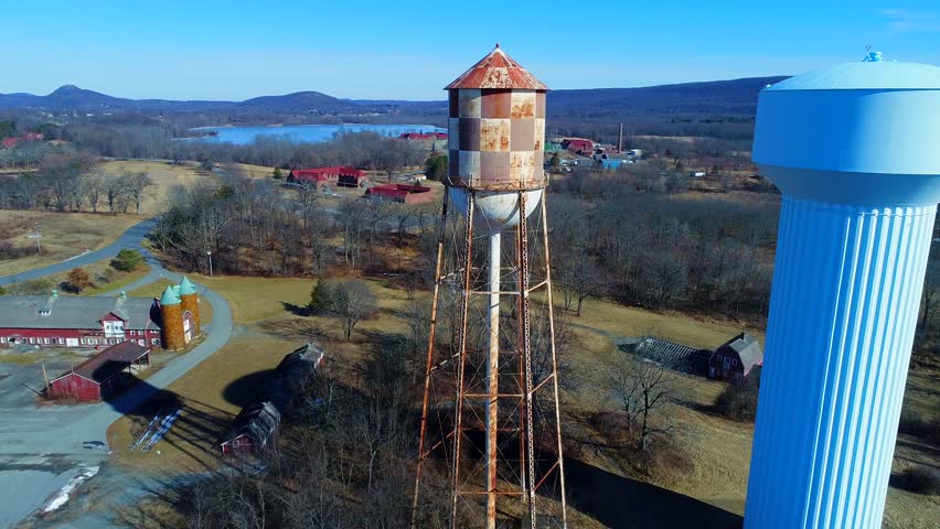 This is an aerial view of two water towers.  One is a modern blue water tower - and the other is an old, rusty checkerboard water tower - located in the beautiful countryside of Warwick, New York.