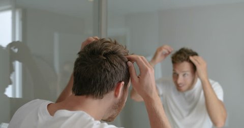 Man looking in bathroom mirror putting wax product touching his hair styling or checking for hair loss problem. Male problem of losing hairs.