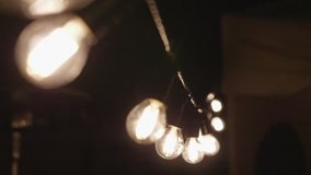 Festival decorative string lights hang and glow outdoors at night. Electric bulbs on a wire moving in slow motion in the dark. Warm lighting, garland of lamps or glass lantern. - Powered by Shutterstock - Get 15% off with code: PIKWIZARD15