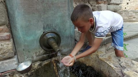 boy drinking water from hands from ancient oriental tap in the old city of Nesebar, Bulgaria