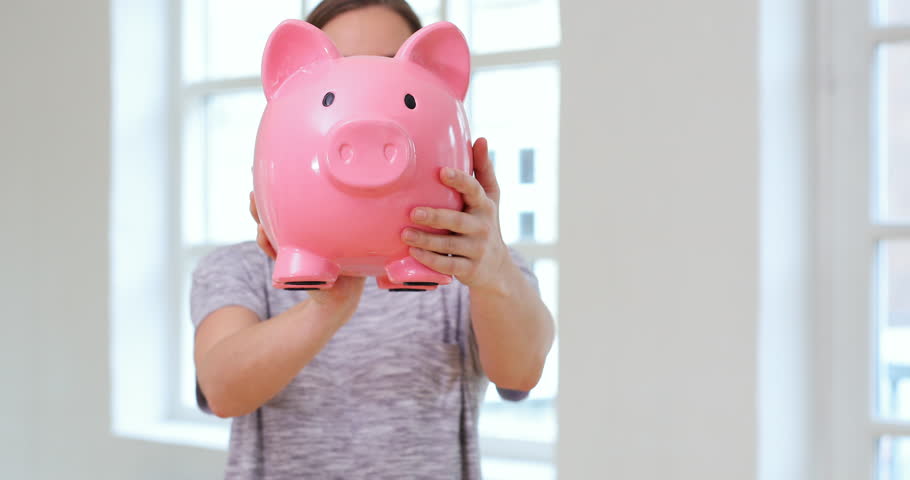 Beautiful woman shaking large piggy bank, smiling