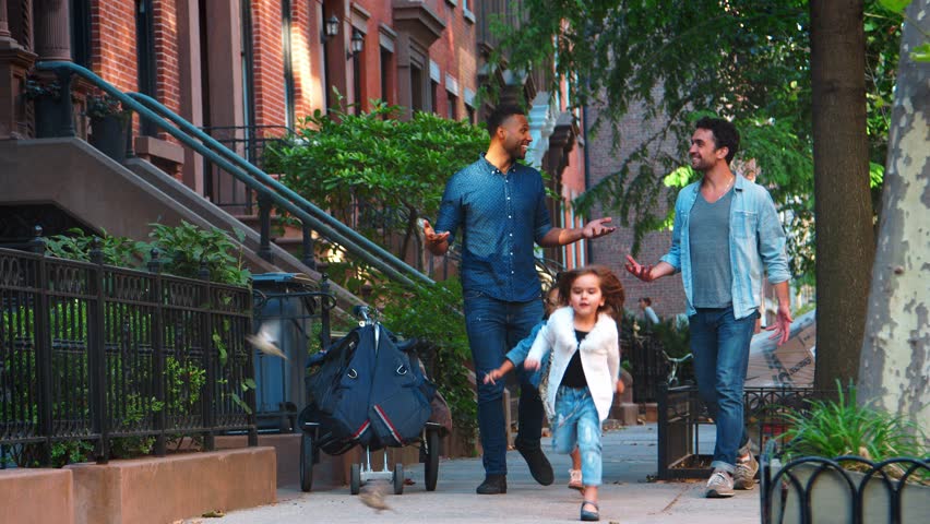 Two fathers with young daughters talking in the street