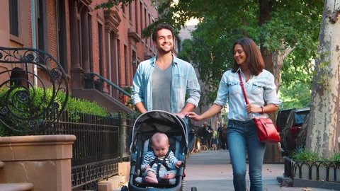 Happy couple walking in the street with baby in a stroller