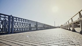 Low angle tracking shot of a businessman riding a bicycle over a bridge towards a bright sun.