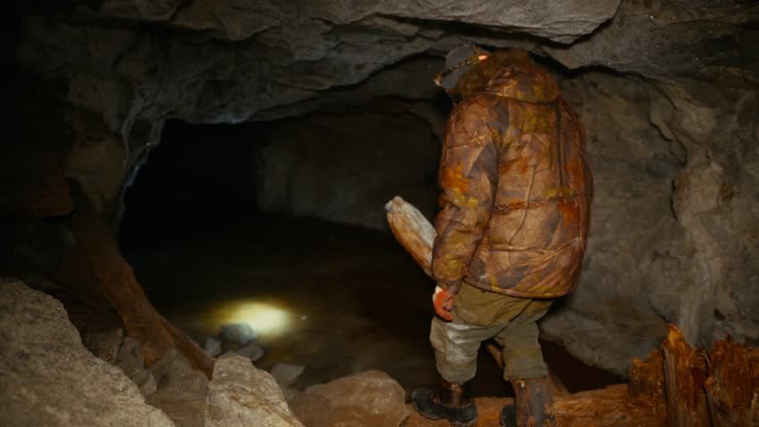 A researcher with a flashlight examines an abandoned mine with collapses