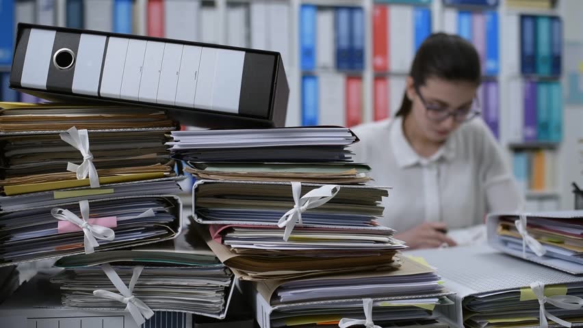 Young woman working in the office and writing documents, she has stacks of paperwork on her desk: work overload concept | Shutterstock HD Video #1007686342