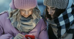 two women outside using smartphone smiling nice girls looking camera happy enjoying technology development emotional glad faces store video winter vacation evening warm clothes fashion style beauty