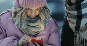 two attractive fashionable girls looking screen smart phone using mobile talking outside winter evening checking news reading text article app notification chat trendy stream beauty hipster woman