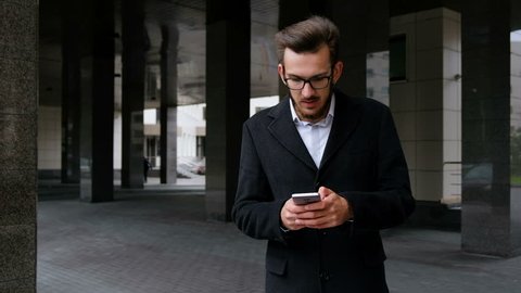 Happy businessman reading good news on smartphone. Young professional man gets news of a successful business deal outside the office