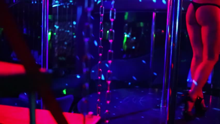 Stripper in panties walks around pole on stage of night club. Slow motion