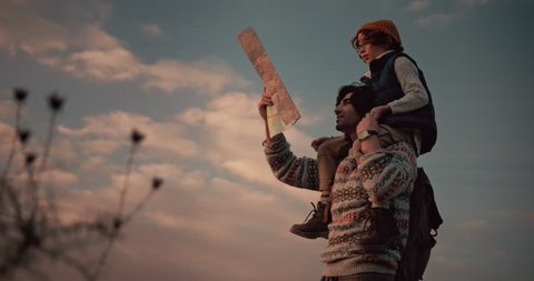 Young son on hiker father's shoulders reading map on trekking and camping adventure on mountains