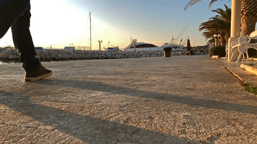 Young man in casual clothes walking on stone shore in harbor on cold winter day slow motion