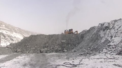 A bulldozer is riding along the edge of the mountain in a career.
The work of heavy equipment in the open development of deposits of fossils.