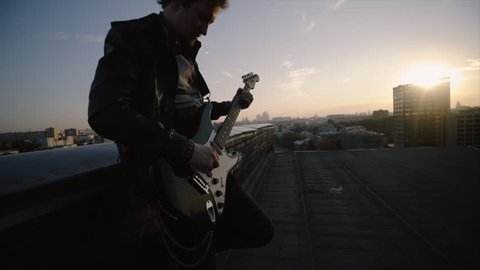 men in rock n roll style standing on the roof and playing on guitar at citiscape background