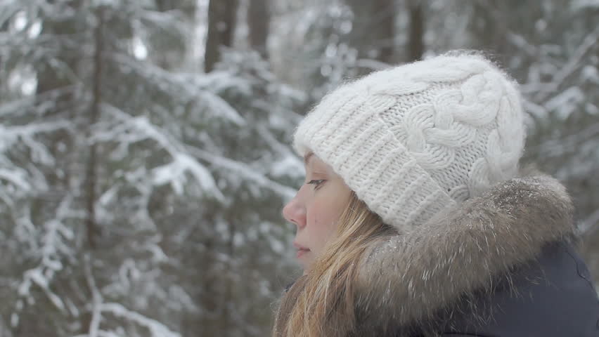 girl in a down jacket with a fur hood walking forward in a winter snowy forest
