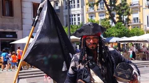 VALENCIA, SPAIN, MAY 21, 2015: Captain Jack Sparrow impersonator with the gun from the Pirates of the Caribbean next to the skull and crossbones symbol on black pirate flag in Valencia, Spain
