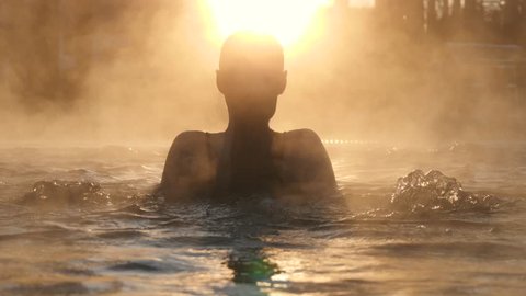 Geothermal spa. Woman relaxing in hot spring pool outdoors. Girl enjoying bathing in a blue water lagoon tourist attraction at sunset. Slow motion