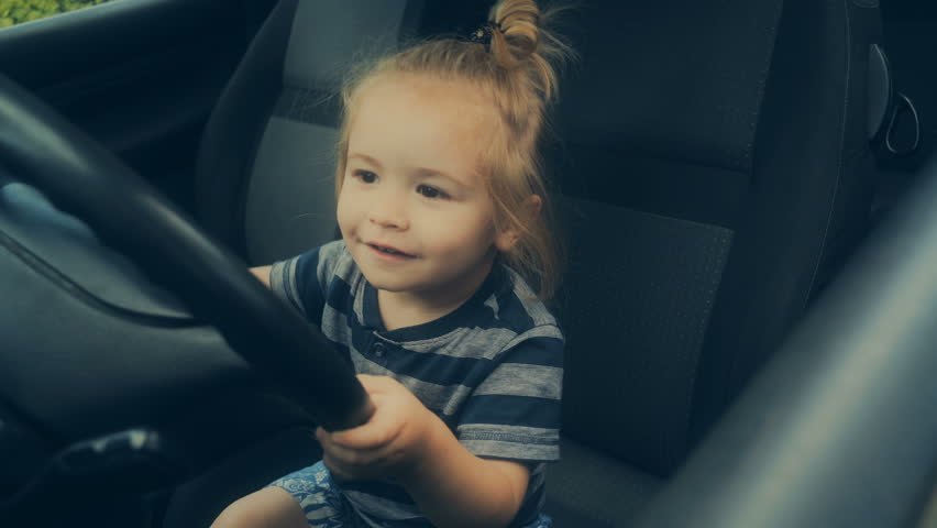 Steering wheel, driving school, driving as a hobby. Boy with long hair likes cars. Cute kid in a daddy car in the front seat. Safety at the wheel. Passenger car for children. Baby on board