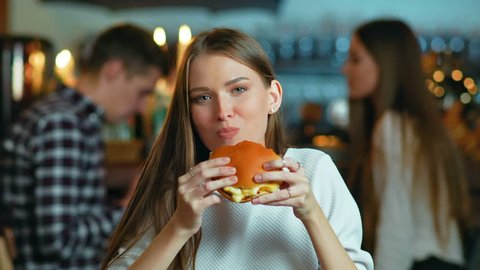 Young happy woman eating tasty fast food burger in cafe