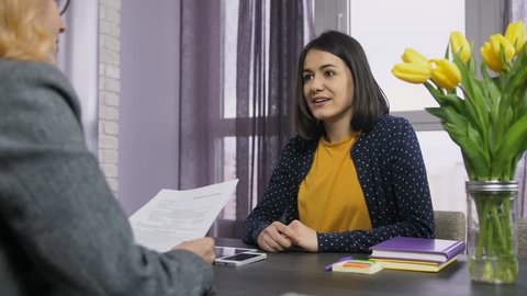 Young female applicant being interviewed by HR manager in office. Brunette woman handing over her CV resume to recruiter and telling about her previous work experience to headhunter.
