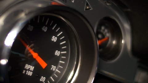 Tachometer of a classic muscle car reacts to hard accelerations by the driver, who is reflected in the glass.
