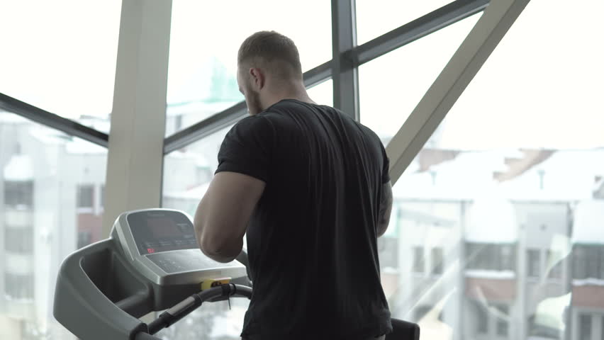 Athletic bearded man with tattoo running on a treadmill close-up 4k.