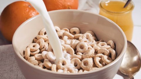 Healthy breakfast of cheerios whole grain cereals with milk, close up. Milk pouring into bowl with honey rings. Pouring milk into a bowl of cornflakes, slow motion.