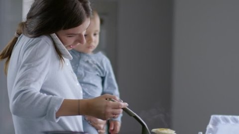 Mother making breakfast for children while holding baby and talking on the phone