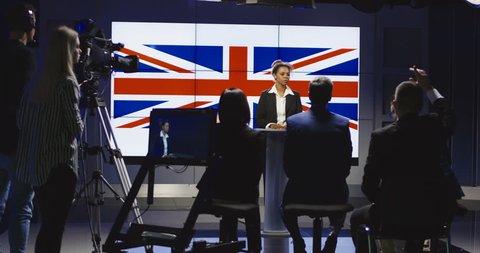 Formal African-American woman as official representative of Great Britain holding speech on press conference against screen with country flag. 4K shot on Red cinema camera.