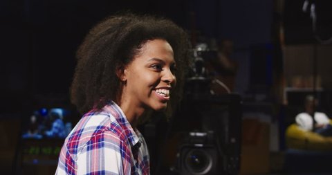 Confident African-American woman in casual shirt sitting in spotlight in telecasting studio and talking while presenting online show.