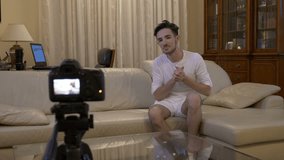 Young social media influencer shooting a new episode on his video blog with a camera at home on couch