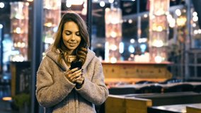 Pleased Brunette woman in coat making selfie on smartphone and showing peace gesture outdoors